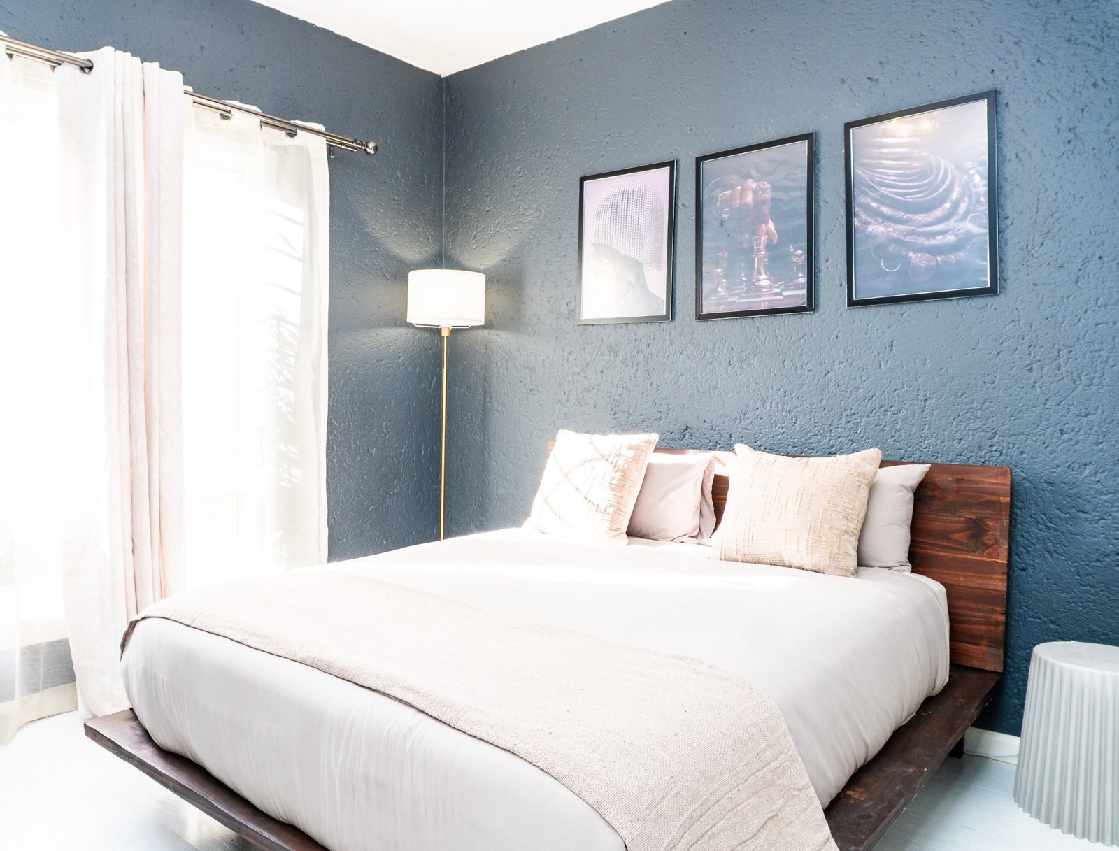 A calm bedroom with a timber bed, cream linen and framed art on a deep blue wall